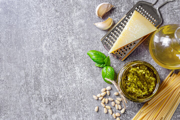 Homemade pesto sauce in small jar and ingredients for pasta on gray concrete background with copy space. Traditional Italian cuisine, recipe, restaurant menu, banner, header