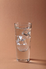 Glass of pure cold sparkling water with ice cubes on light brown background