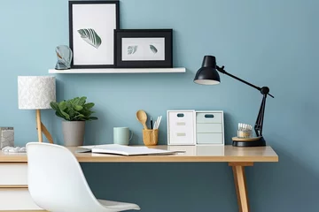 Fotobehang Desk at home office with blue wall, supplies, picture frame, and extras. Close up of a stylish interior table with a laptop and office supplies. Banner © Vusal