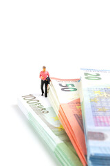 Miniature businessman navigates the financial landscape, surrounded by Euro banknotes, embodying the essence of success and prosperity on a small but impactful scale.