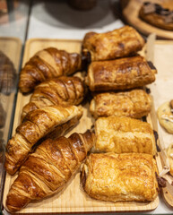 Fresh baked croissants and pastries on wooden tray, vertical photo.