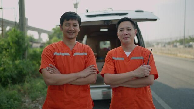 Portrait of two paramedics man. Two asian paramedic man in uniform standing with arms crossed rear of the ambulance smiling to camera. EMS Paramedic