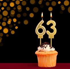 Birthday candle with cupcake - Number 63 on black background with out of focus lights