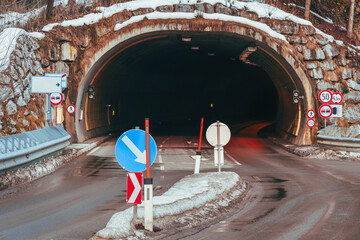 The view of the entrance to a tunnel on a highway in the Alps on a winter's day, decorated with road signs, exudes an atmosphere of mystery and exploration. Travel, transition or path concept