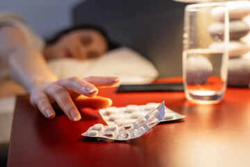 Defocused woman reaches for red bedside table with medicines, hand and sleeping pills in close-up....