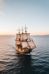 Obraz premium Small sailing ship in the open sea at sunset. The Golden Horizon, a magnificent vessel from the 17th century, adorned with golden accents and a grandeur that captures the imagination.