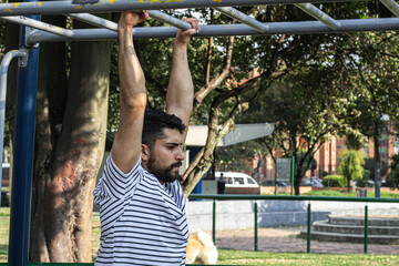 Fototapeta premium attractive young man exercising on bar in a park outdoors training arm strength exercise