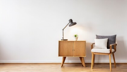 desk lamp on a small table and a simple wooden cabinet in an empty living room interior with white wall and place for a sofa real photo