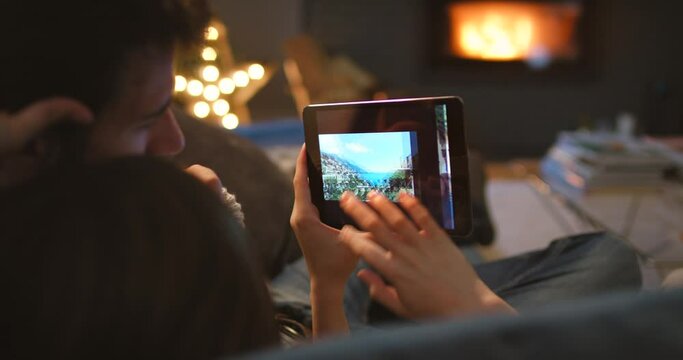 Hands, tablet photograph and memory with couple on sofa in living room of home from back at night. Technology, love or travel pictures with man and woman browsing online album of vacation or holiday