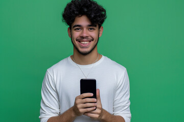 Smiling young Latin man holding a smartphone on a green background