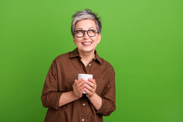 Portrait of pleasant person with gray hairstyle hold cup of tea look at proposition empty space isolated on green color background