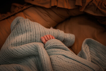 A baby's foot covered with a blanket in warm lighting. The concept of health and warmth in rooms where children stay especially in winter. The concept of raising toddlers and caring for them.