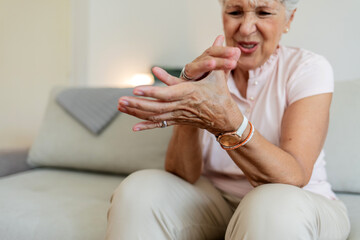 happy senior old hoary woman touching wrist joint, suffering from injured hand. Frustrated stressed...