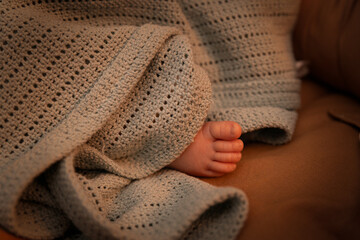 A baby's foot covered with a blanket in warm lighting. The concept of health and warmth in rooms where children stay especially in winter.