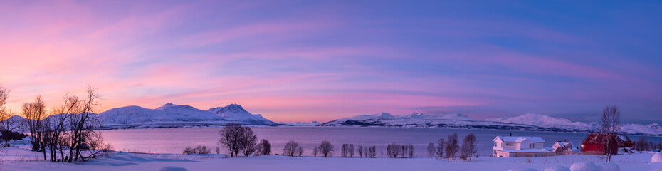 Panoramic view of a Norwegian fjord at twilight featuring a traditional red house amidst a snowy landscape near Tromsø, Norway. © Ludovic Charlet