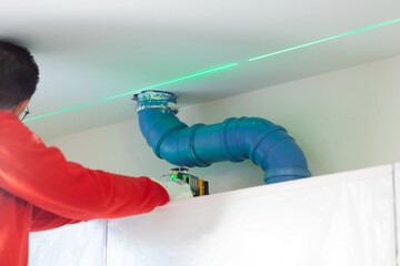 A plasterer takes measurements with a laser level to create a wall above the kitchen cabinets. - 724760868