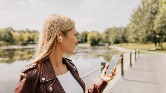 Young caucasian girl with wireless headphones in the park using tablet, phone and smiling