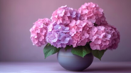  a gray vase filled with pink flowers on top of a purple tableclothed tablecloth and a pink wall behind the vase is a gray vase with pink flowers and green leaves.