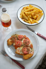 chicken breaded schnitzel with tomato and cheese with French fries and a glass of beer.