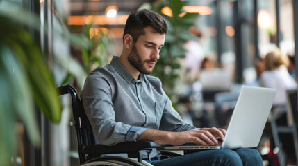 Portrait of disabled male office worker in a wheelchair looking at the screen of his laptop while performing in co-working space