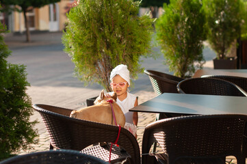 Little cute girl with french bulldog in a chair on the terrace of a cafe in the middle of the city