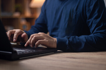 Businessman in blue long-sleeved t-shirt works in modern loft office at night.