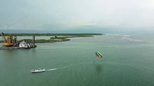 Aerial view of parasailing over the ocean at Benoa Bay, Bali. Water sports and water activities on vacation. Motorboat with a parachute tied to it, extreme entertainment.