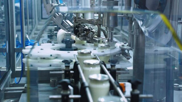 A packaging machine at a dairy factory automatically screws caps onto glass jars of milk or yogurt. Packing and bottling of dairy products. Vacuum modern packaging of food products
