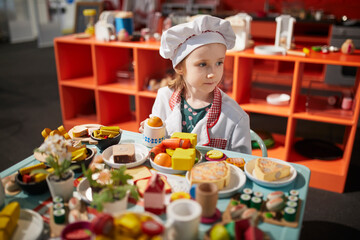Adorable preschooler girl playing cook at the kitchen or in restaurant