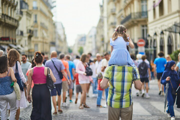 Father holding daughter on shoulders and walking on a street of Paris, France