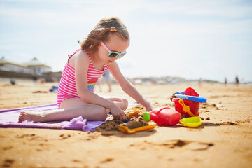 Adorable preschooler girl playing on the sand beach at Atlantic coast of Brittany, France
