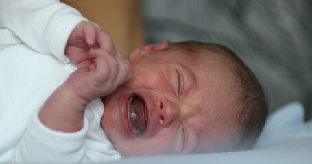 Newborn baby infant crying laying in bed, close-up of baby face crying