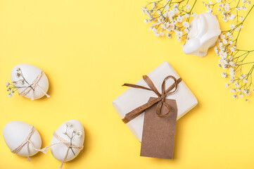 Easter eggs decorated with twine with sprigs of gypsophila and a gift box on a yellow background....