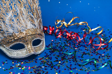 Golden Mardi Gras or carnival face mask on a blue background with colored tinsel and confetti....