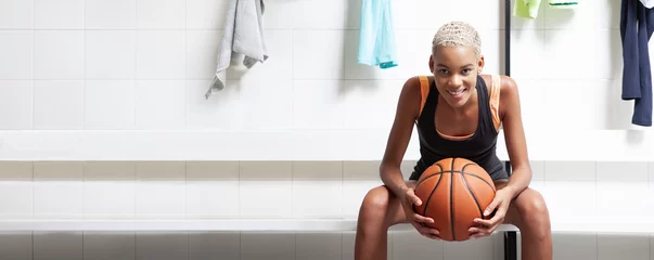 Fotobehang Sport basketball player in the locker room, a smiling African American female athlete holding the ball before the game, competition or training. Woman sitting in changing room with basket ball © amedeoemaja