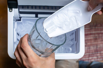 Closeup shot of a person's hand transferring bullet type ice cubes from a small portable ice maker...