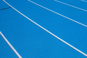 Blue Stadium track lanes with white stripes, an empty background suitable for copy space, represent the concept of physical sports and running, symbolizing commitment and pathways towards goals