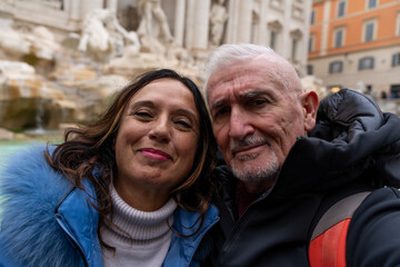 happy middle aged couple on vacation taking a selfie in front of a famous trevi fountain in rome