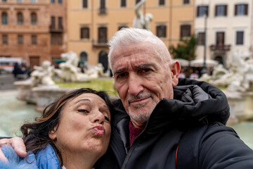 happy middle aged couple of tourist on vacation taking a selfie in front of a famous navona square in rome