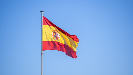 Spanish flag waves in the wind against a blue sky, banner blowing like soft silk