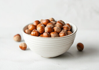 hazelnuts in a white ceramic bowl, centered, with a soft focus on the nuts outside the bowl, on a white background