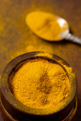 in the foreground, in a wooden container, some organic turmeric powder. - 724838473