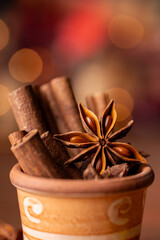 In the foreground, in a colored earthenware jar, some cinnamon sticks and an anise star, lights on a bokeh background. Still life - 724839020