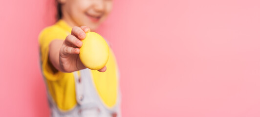 Little girl holding a yellow Easter egg in her hand against a pink background.