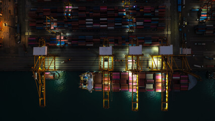 night scene shot from above commercial port loading and unloading cargo from container ship import and export by crane for distributing goods by trailers transported to customers and dealers.