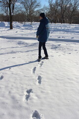 a boy in a blue jacket walks and leaves footprints on white snow in the forest in winter