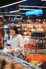 Young woman with a shopping bag as a customer buying fish at the refrigerated shelf in the supermarket