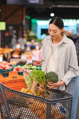 Young woman chooses broccoli, buying vegetables in supermarket.