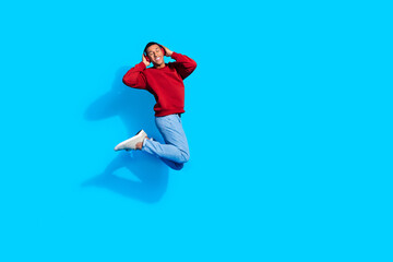 Photo of joyful positive man wear red trendy sweatshirt listen music wireless headphones empty space isolated on blue color background