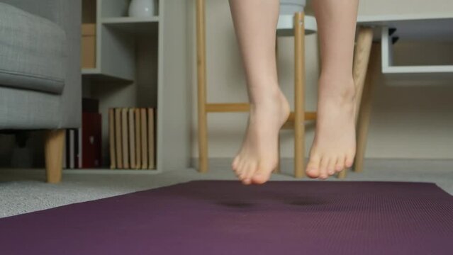 Child jumping barefoot on yoga mat, feet close-up. Childrens sports at home